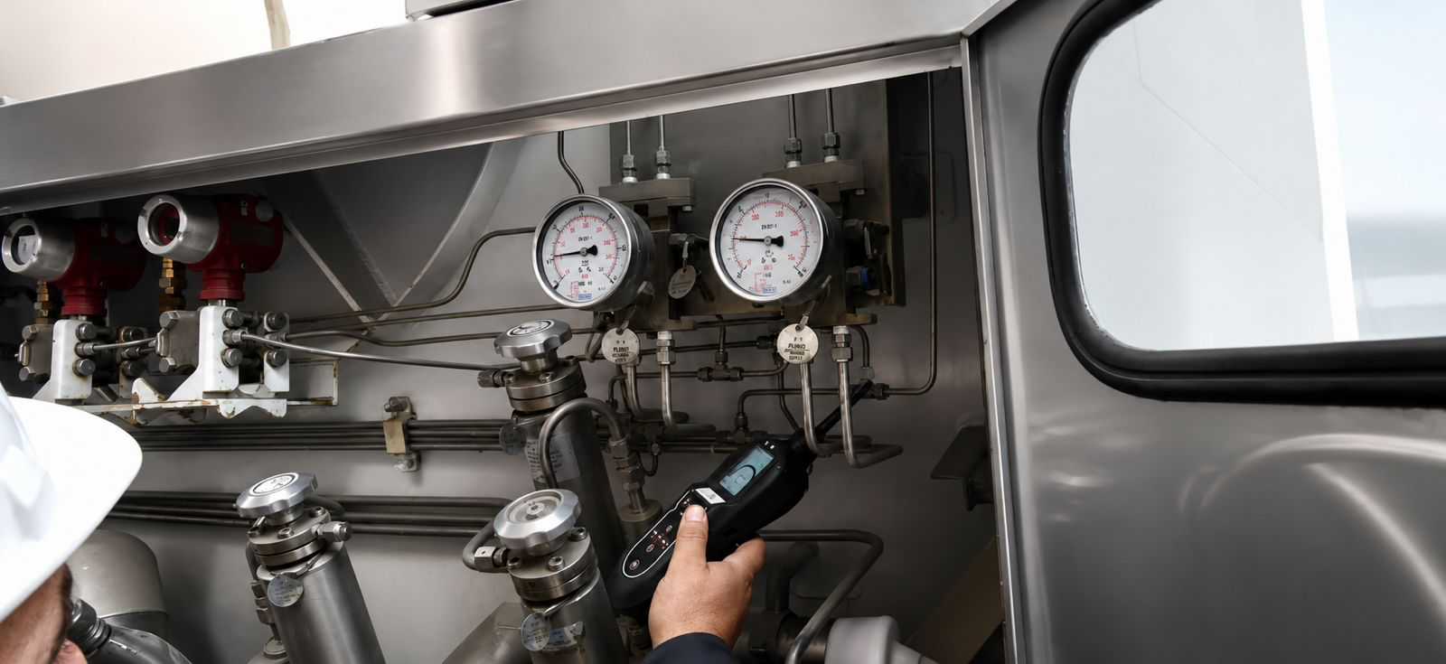 Technician examining valves, gauges and pressure-control tubing with a handheld detector
